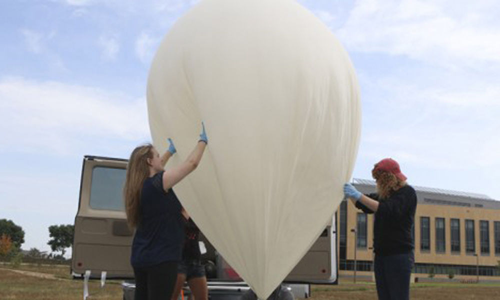 Professor Erick Agrimson inflating a weather balloon, while his students hold it steady. Photo by Ashley de los Reyes '15