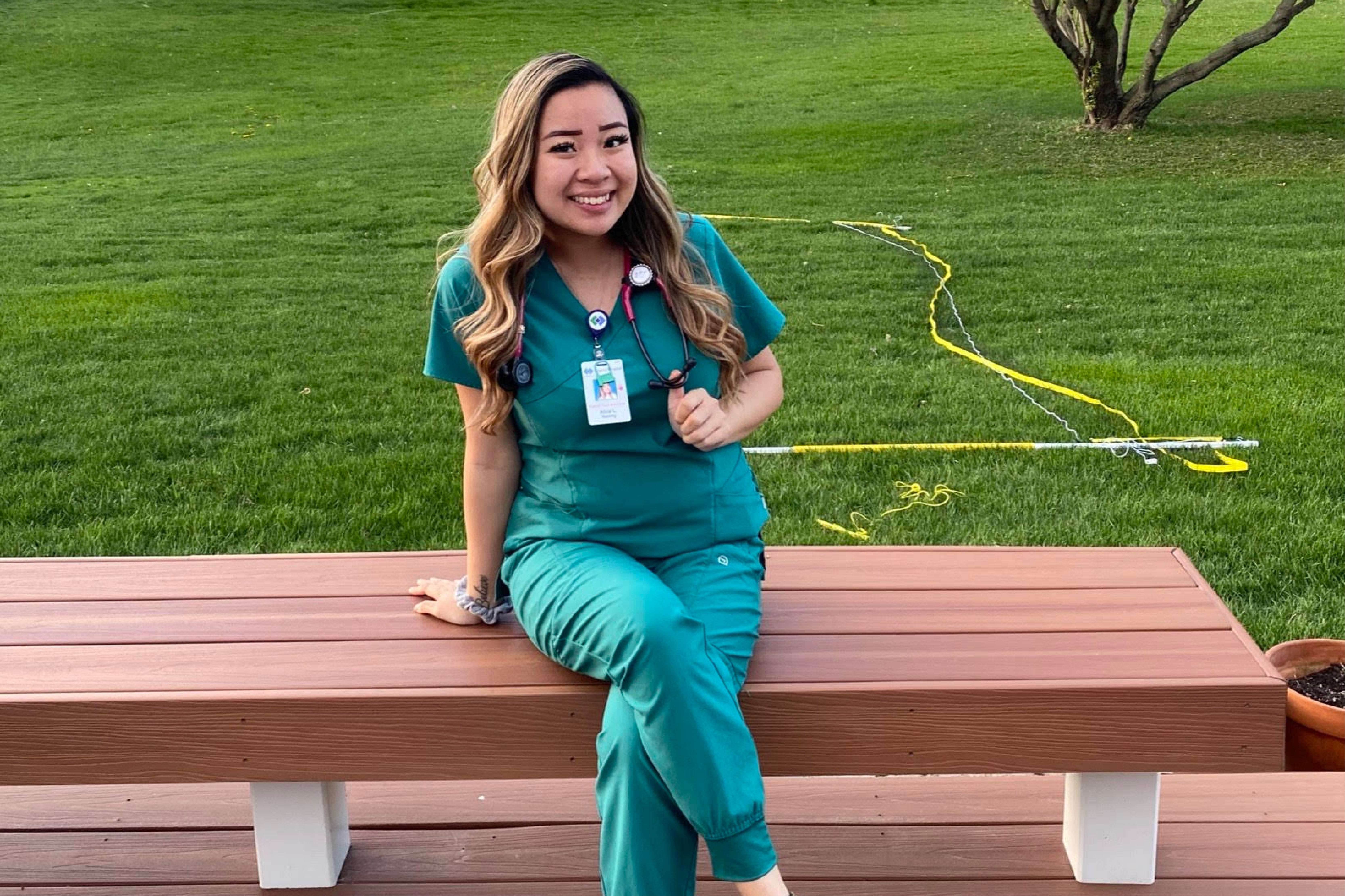 Respiratory Care undergraduate student Alice Le'22 on a bench outside in her green scrubs