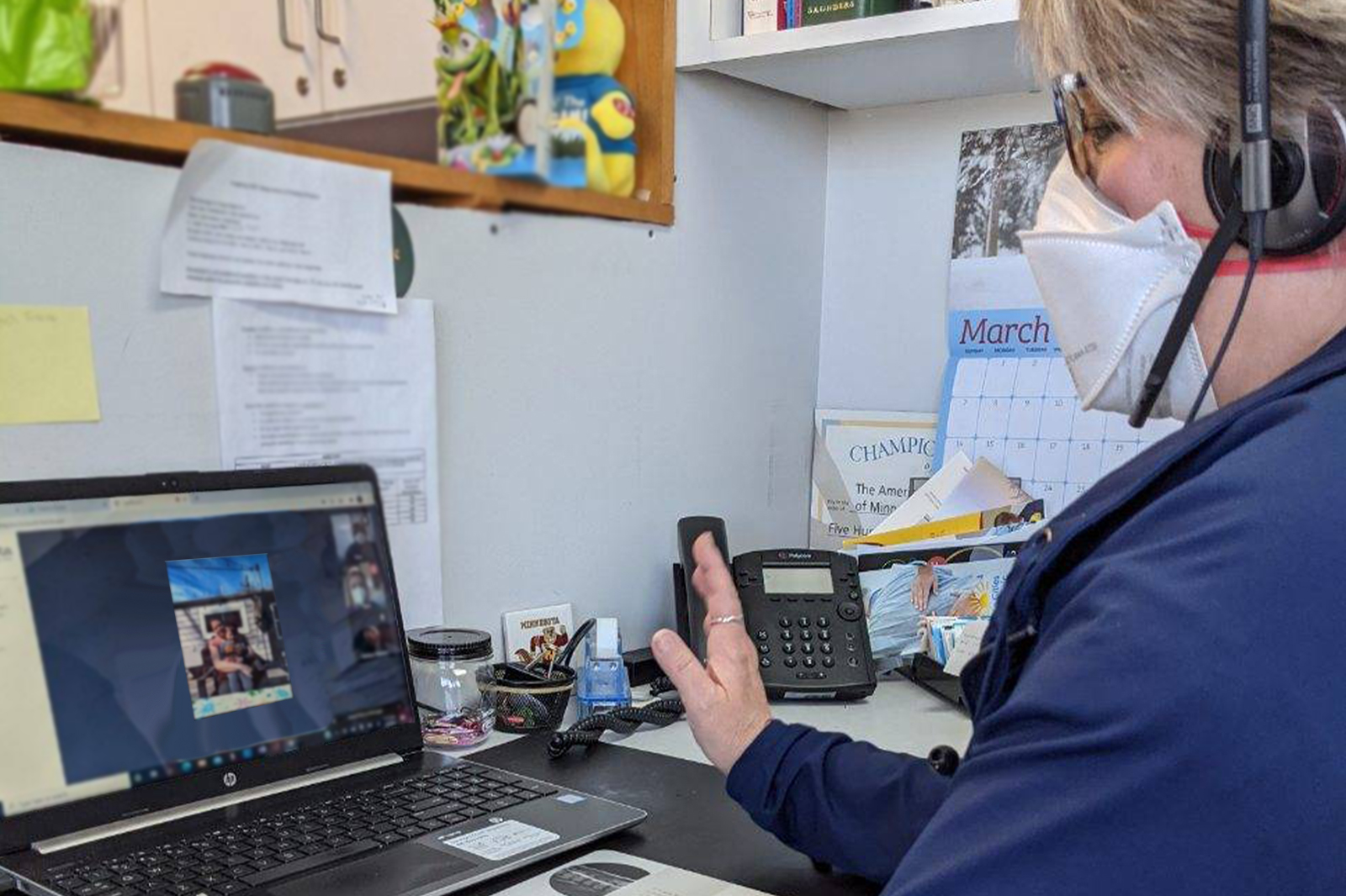 Wearing a face mask and a headset, St. Kate’s Professor of Nursing Gretchen Moen, DNP, APRN, CPNP-PC, on a telehealth visit in front of a computer.