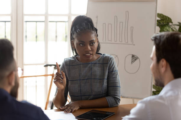 A sales manager in business attire leads a discussion with a sales team at a conference table.