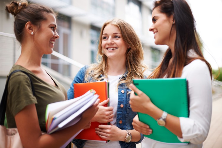 Group of women college students talking and smiling on campus.