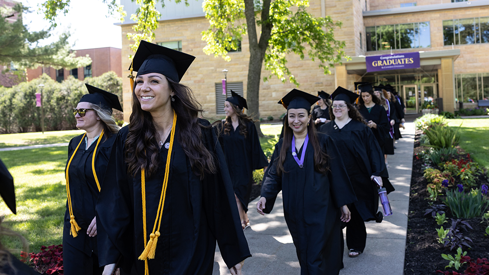 A group of new graduates in cap and gown in a procession outside.