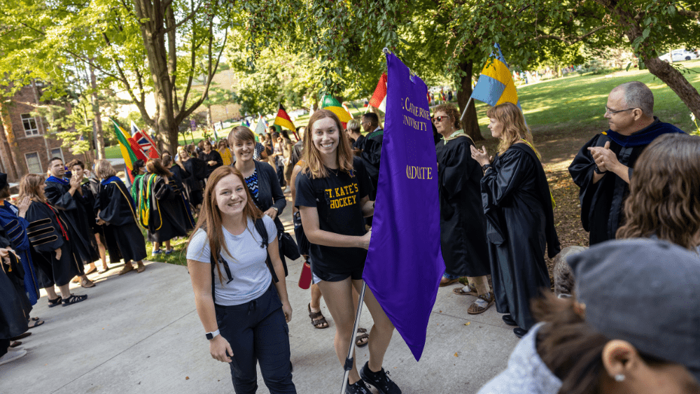Two people walk with a purple banner that reads "Graduate"