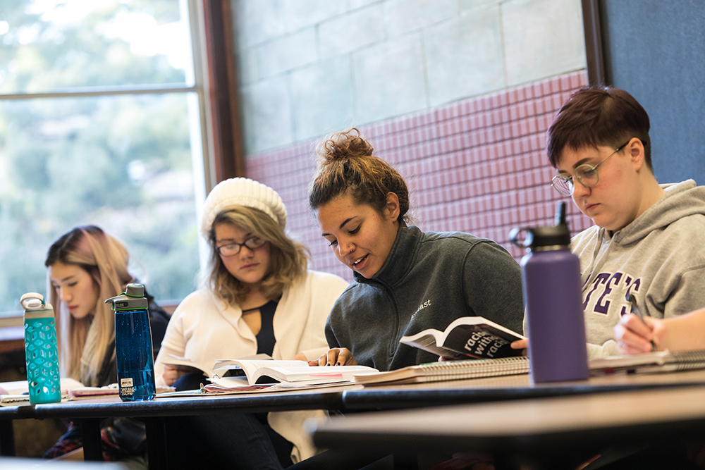 Four students sitting in a class following along in a reading
