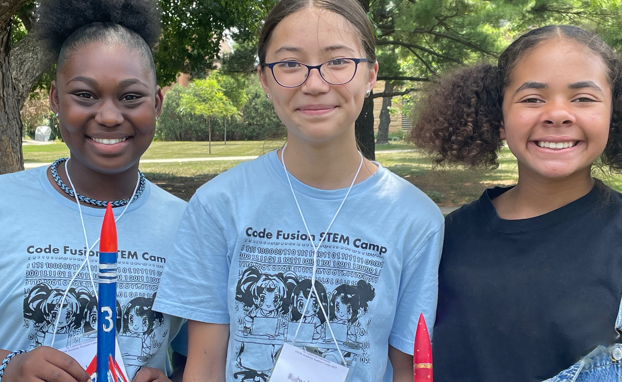 Three STEM camp attendees posing for picture with model rockets