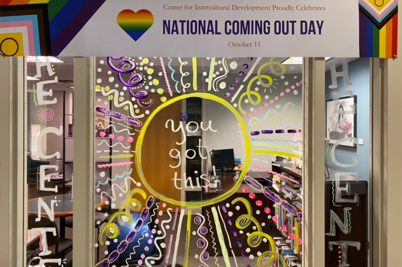 Colorful painted window to Queer Resource office with the words "You got this!" in the middle of window