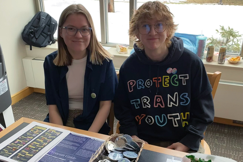 Two students sitting at information table posing for picture