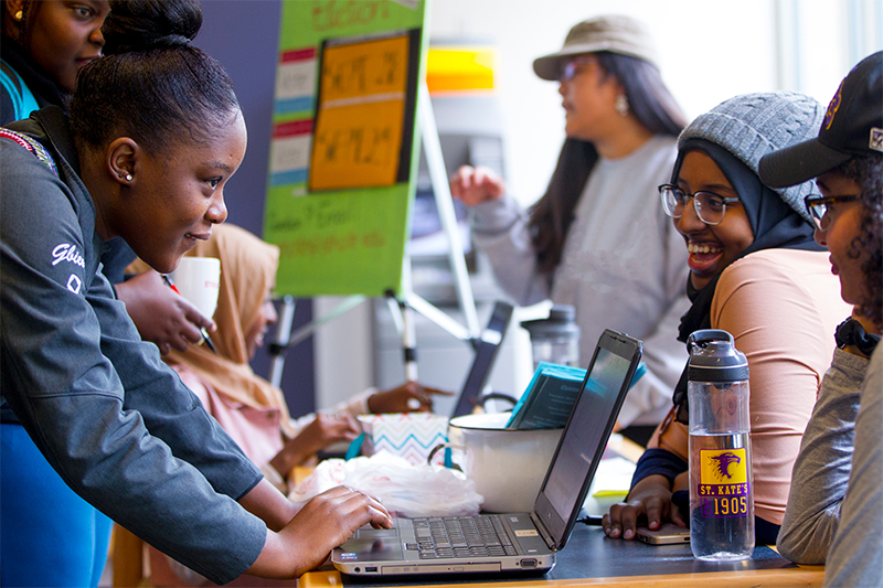 student women collaborating around laptop for school