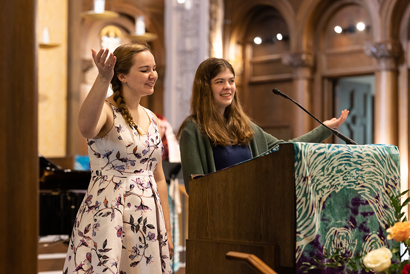 Two women at alter leading chapel in song