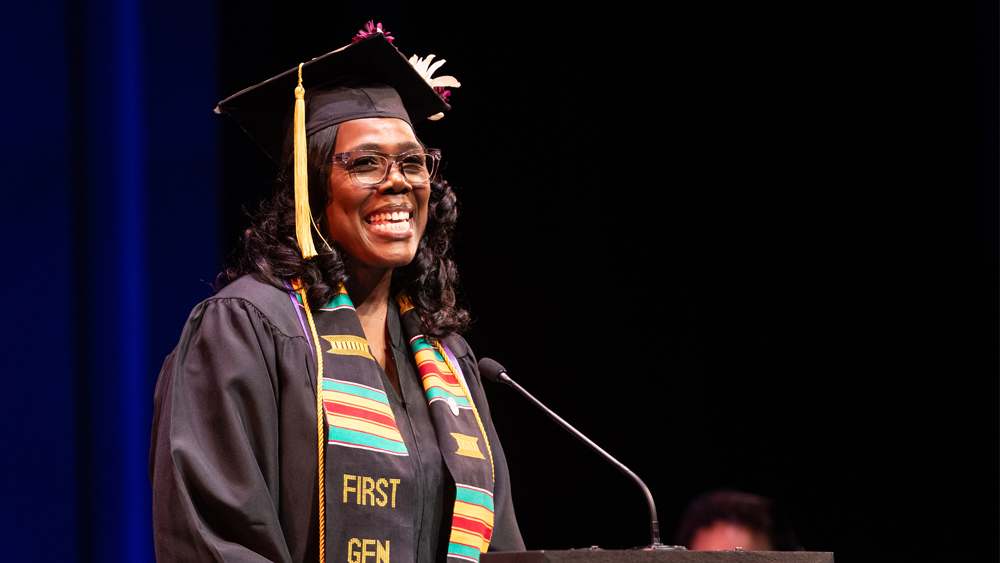 A person wearing a graduation cap and gown stands in front of a microphone.