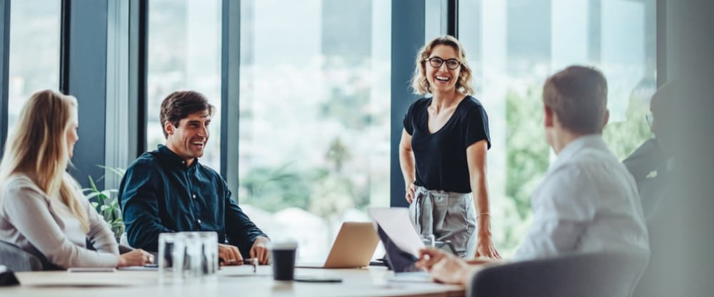 A smiling team of colleagues discusses business strategies in a modern office meeting room. 