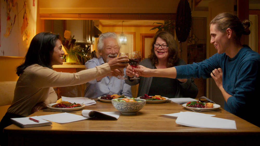 four people sitting at a dinner table clicking glasses