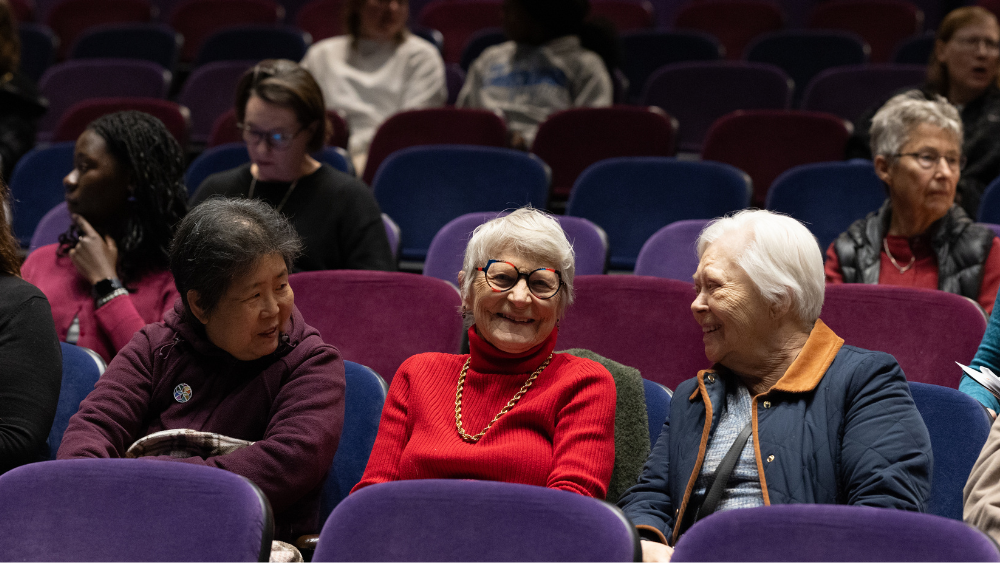 three women sitting in the auditorium smiling and chatting