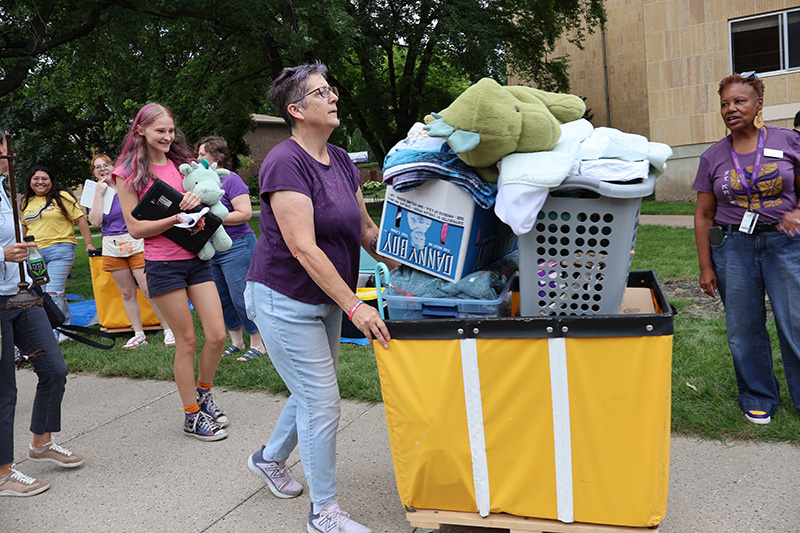 Faculty helping students move in carts of stuff into dorms