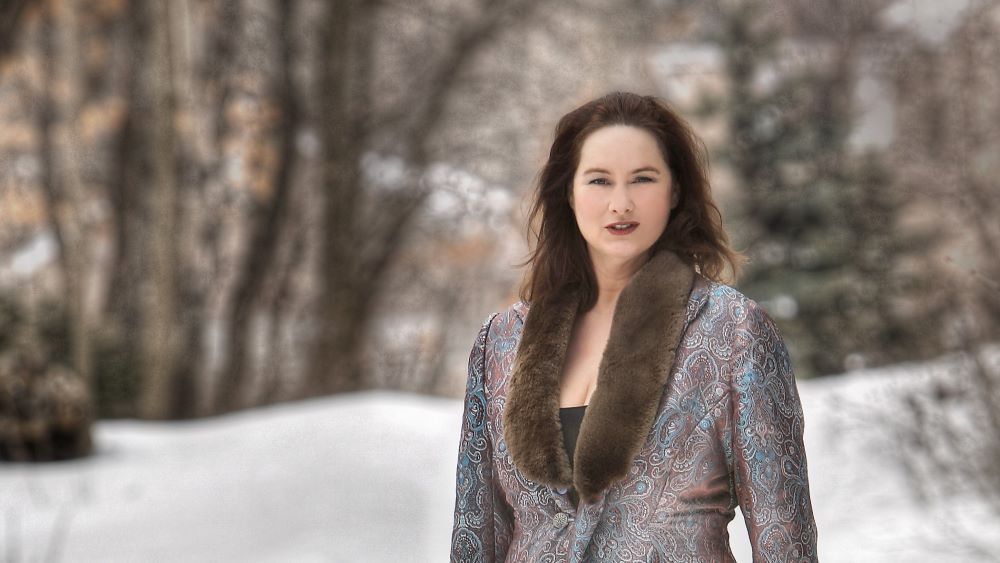 Portrait of Katie McMahon with a fur collar coat against a snowy wooded background. 