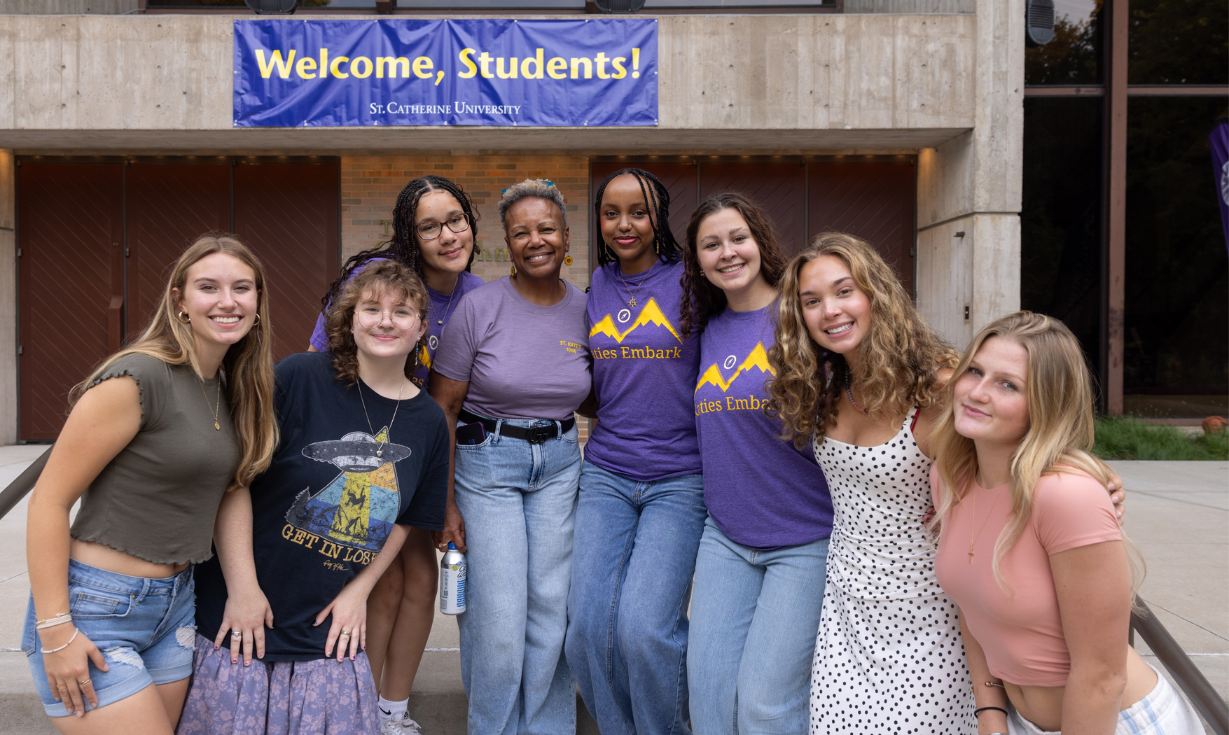 President Evans poses with a group of students in front a sign that reads "Welcome, Students!"