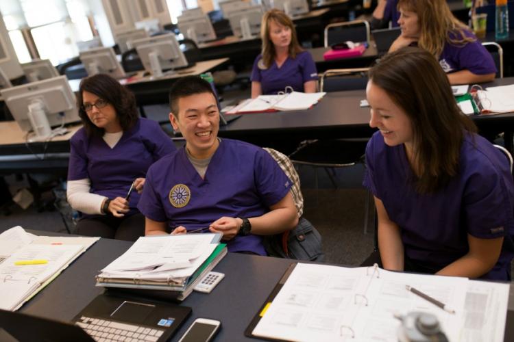 Students in a Holistic Nursing class: study materials are on the table in front of them, and two of the students are smiling and discussing something.
