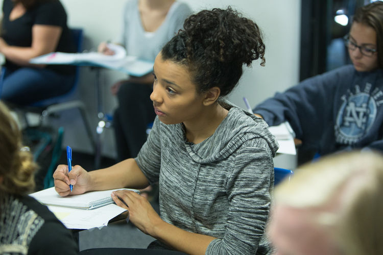 Student taking notes in class with a question