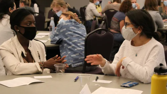 Two students seated at table discuss during IPE forum.