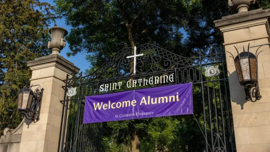 A banner with the words "Welcome Alumni" hangs from the open gates of St. Catherine University