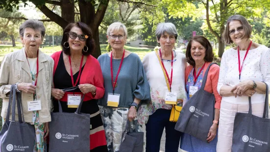 Alumni with matching complimentary tote bags smile at Reunion