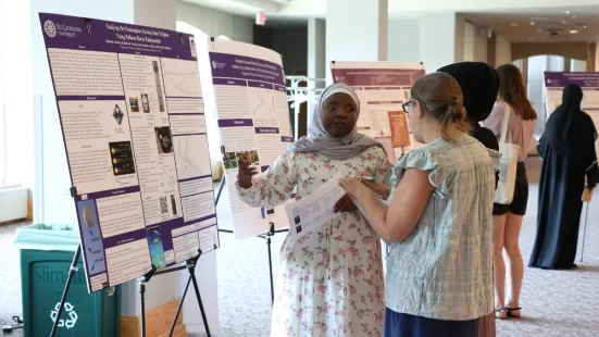 A student standing in front of a poster explains their research. 