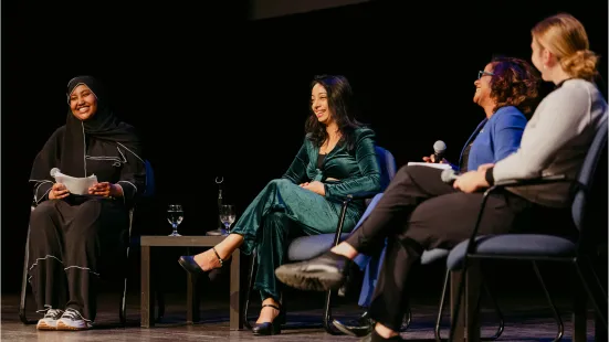 A panel of four women sit on stage and talk. 