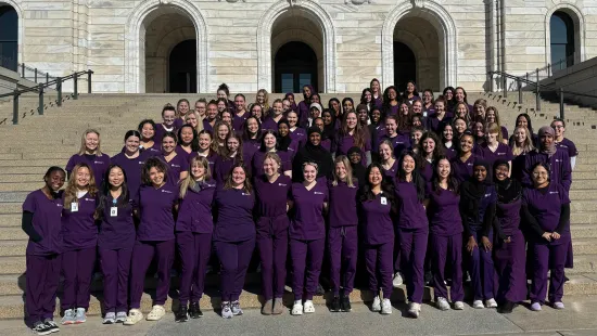 A large group of nursing students in purple scrubs stand outside the Capitol.