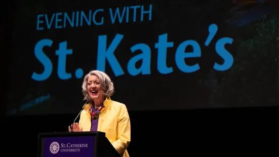 President Roloff speaks at a podium in front of a projected screen that reads "Evening With St. Kate's"