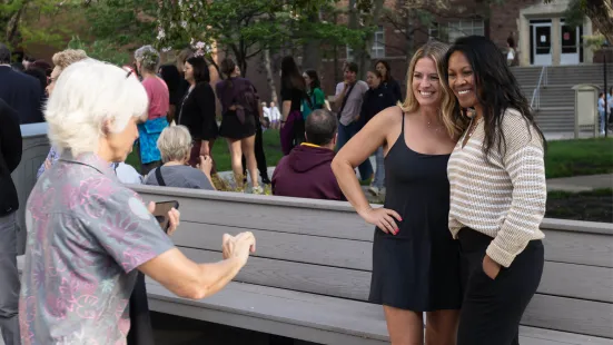 Two women on the right pose for a photograph while another person holding a phone directs them.