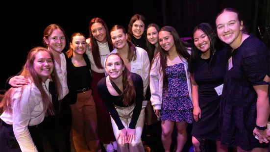 A large group of people stand and pose together inside, in front of a black curtain.