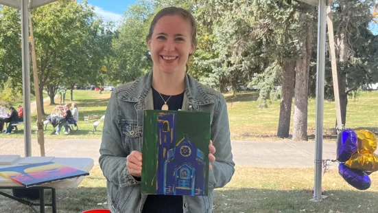 A person wearing a jean jacket holds up a painting of the Chapel.