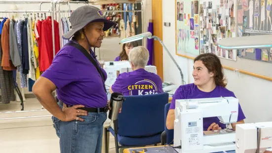 President Marcheta P. Evans standing by a student sitting at a sewing machine. There is another student working on a sewing machine in the background.