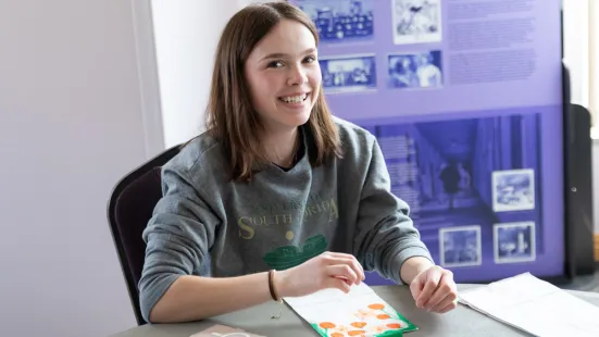 A smiling students looks up from painting a paper bag.