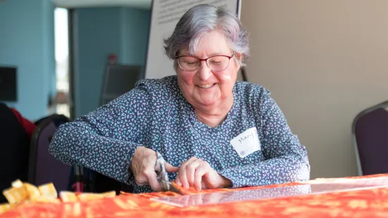 A woman uses scissors to cut orange fabric.