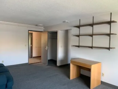 Alberta apartments living room with TV stand, shelving furnishings, angled to show the entrance doorway.