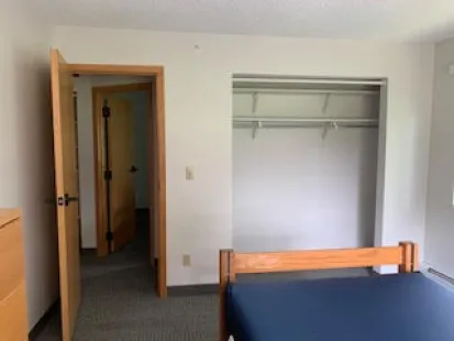 An example of a partially furnished bedroom in the Georgia and Alberta apartments, including a bed, desk, and dresser. Angle includes a view of the closet.