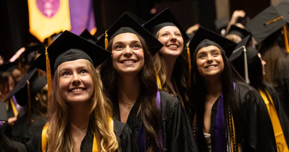 Graduates wearing caps and gowns look up and smile.