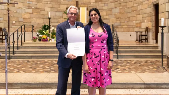 A man wearing a suit and a woman in a pink dress smile in front of an altar.