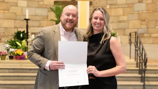 A man and a woman smile and hold up a paper certificate. 