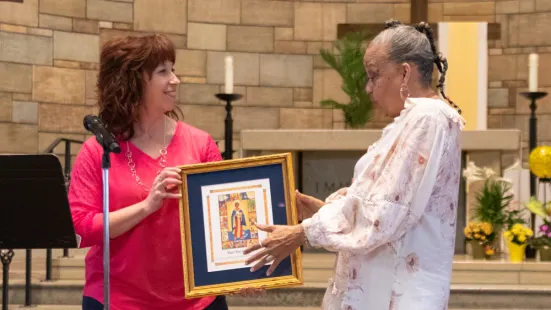 Two women hold up a framed piece of art between them and smile.