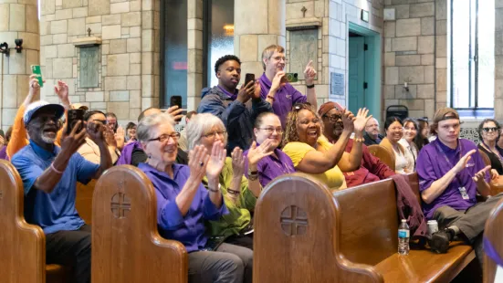 People sitting in pews clap and cheer.