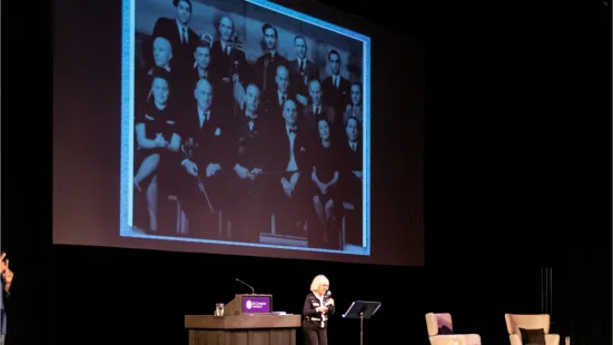 Janet Horvath speaks onstage, displaying archival photos onscreen