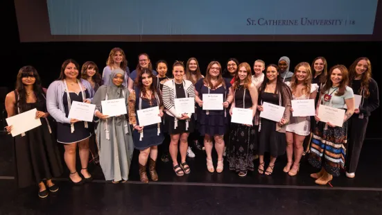 A group of students, each holding a paper certificate, stands on stage.