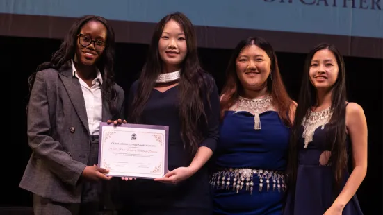 Four students stand on stage; two of them hold a certificate between them. 