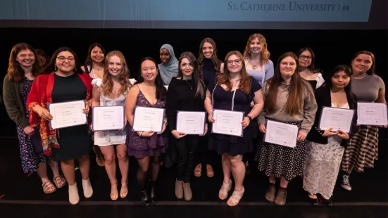 A large group of students stands on stage, each holding a paper certificate. 