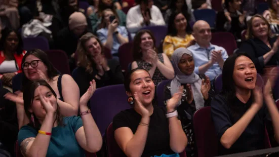 A group of people sitting in the audience smile and clap their hands.