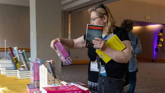 A woman holding a stack of books examines a book on display.