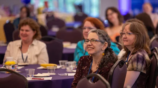 A group of women sitting at tables with purple cloth.