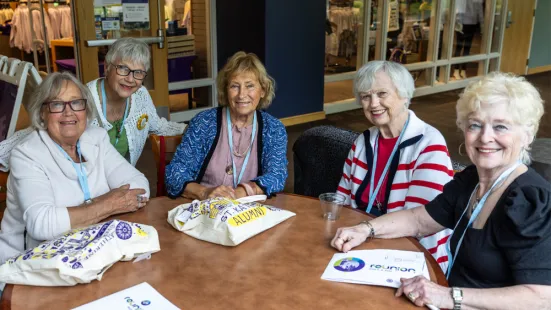 A group of women wearing lanyards sit around a table and smile.